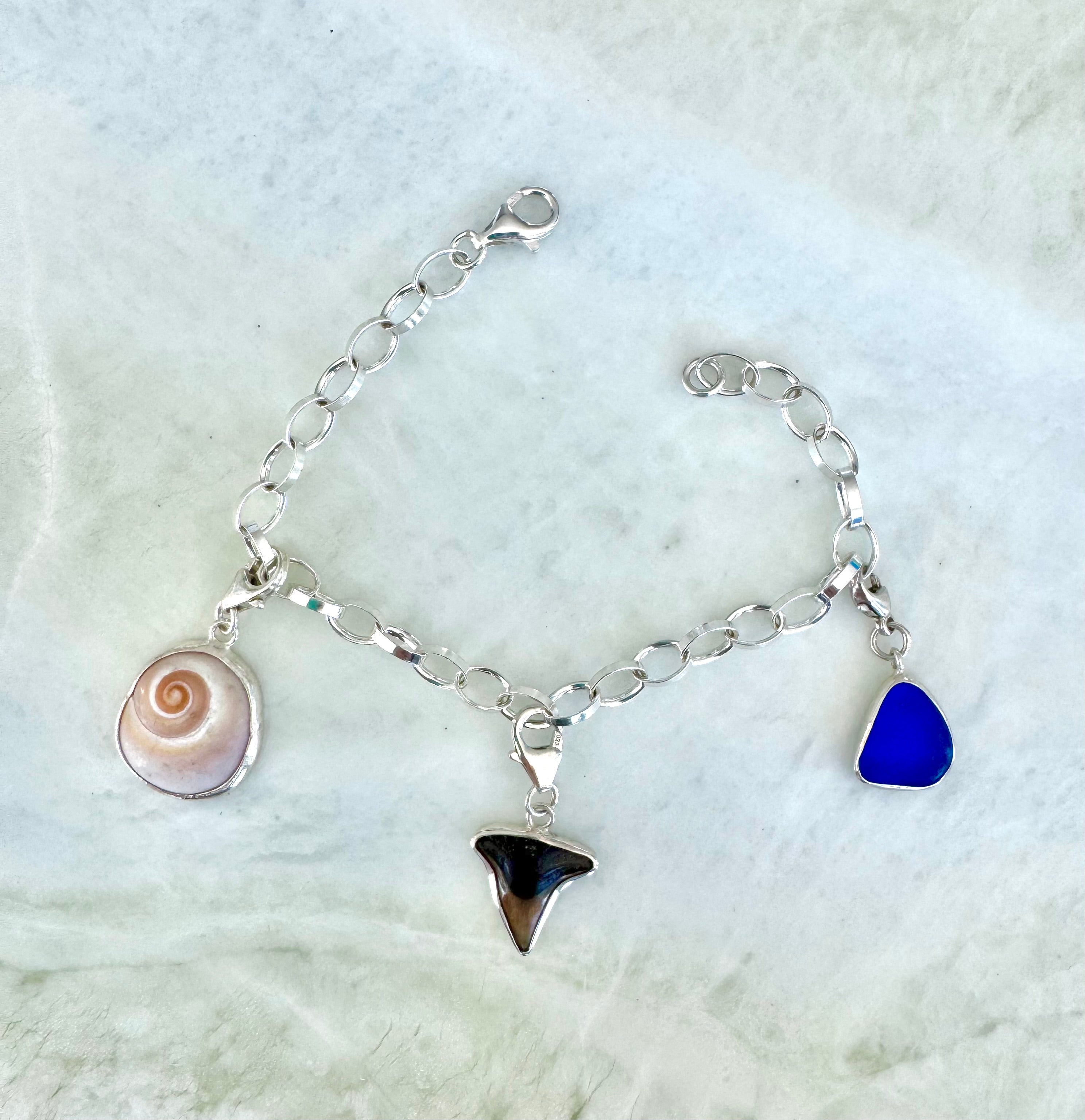 Sterling silver rolo link charm bracelet featuring cobalt blue sea glass from Spain, shark eye shell, and fossilized shark tooth from Casey Key, Florida.