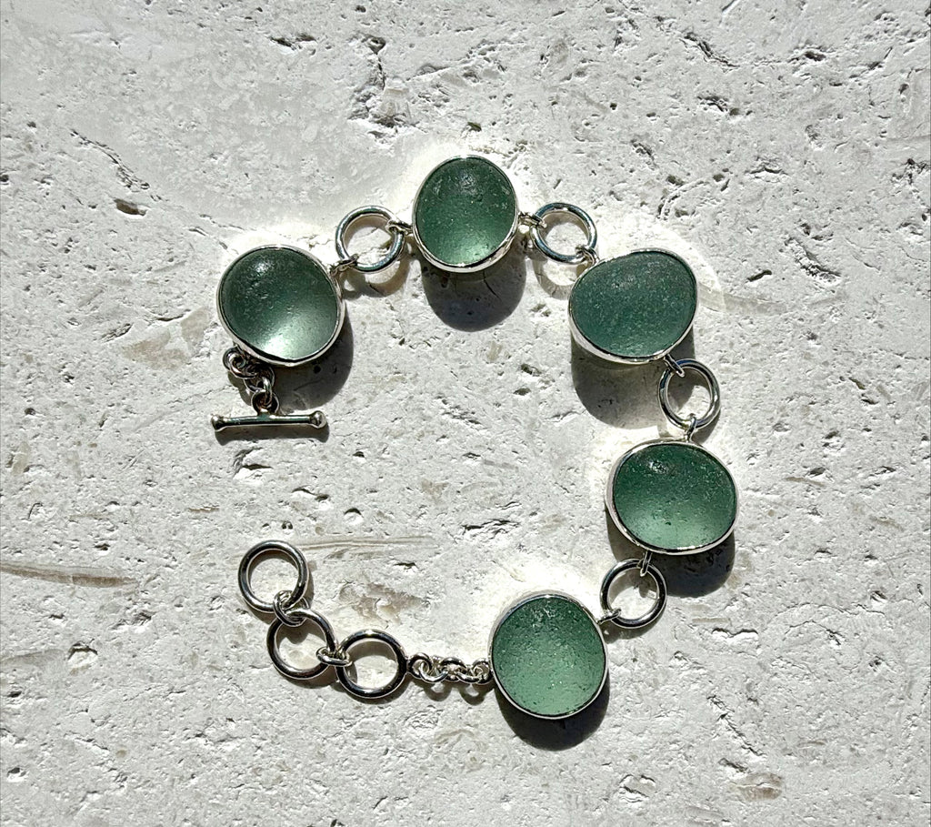 Bracelet with green circular sea glass on a textured surface