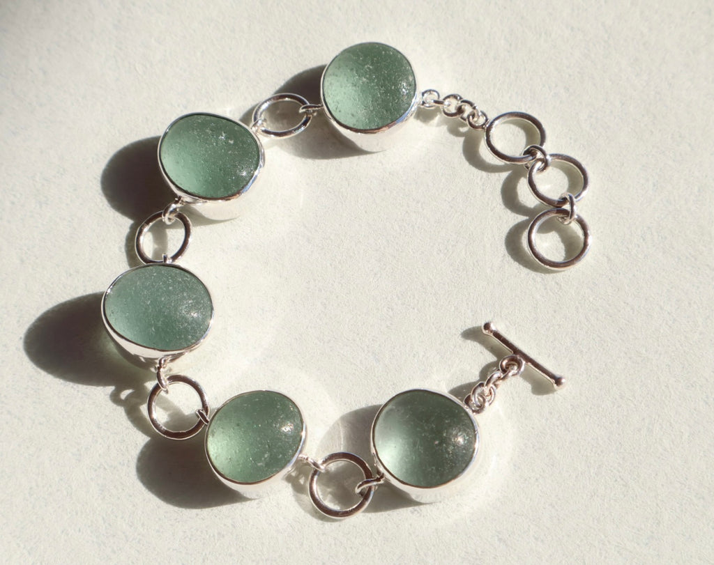 Bracelet with green circular sea glass and silver links on a light background