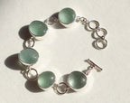 Bracelet with green circular sea glass and silver links on a light background