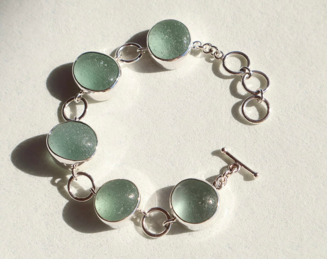 Bracelet with green circular sea glass and silver links on a light background