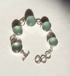 Bracelet with green circular sea glass and silver chain on a light gray background