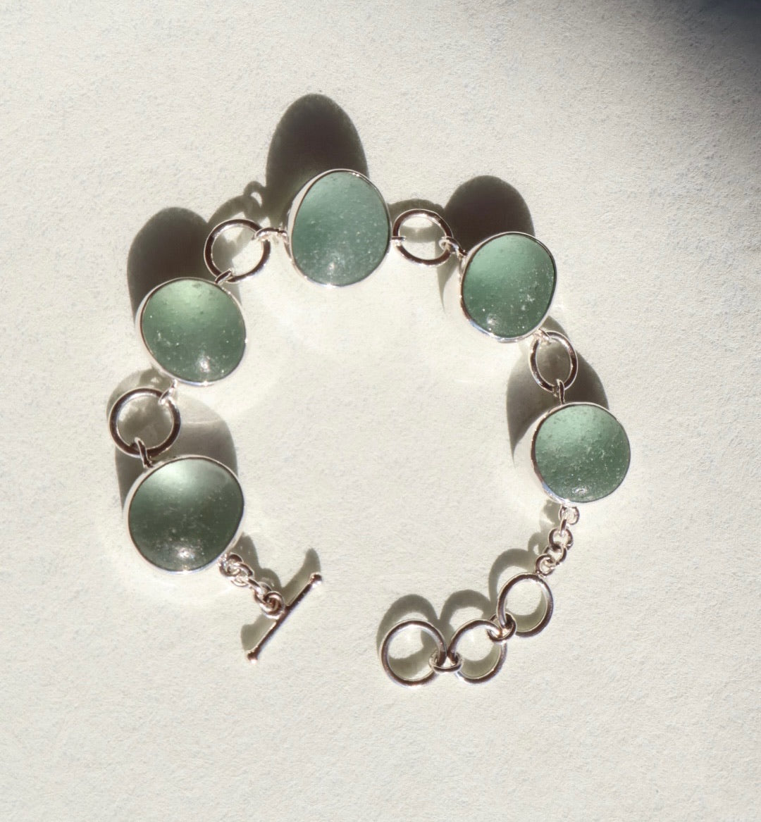 Bracelet with green circular sea glass and silver chain on a light gray background