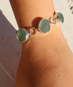 Bracelet with green circular sea glass and silver accents on a wrist.