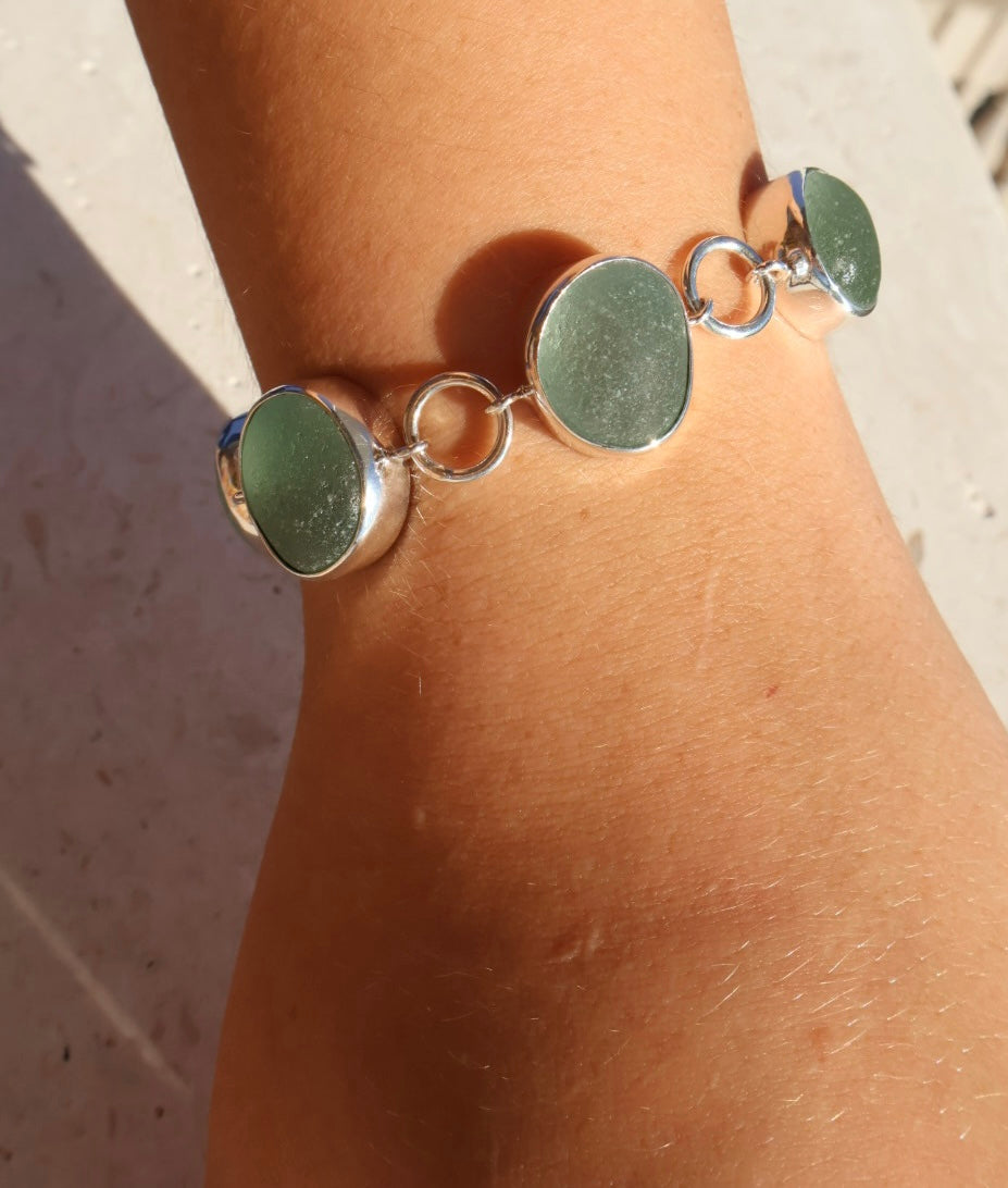 Bracelet with green circular sea glass and silver accents on a wrist.