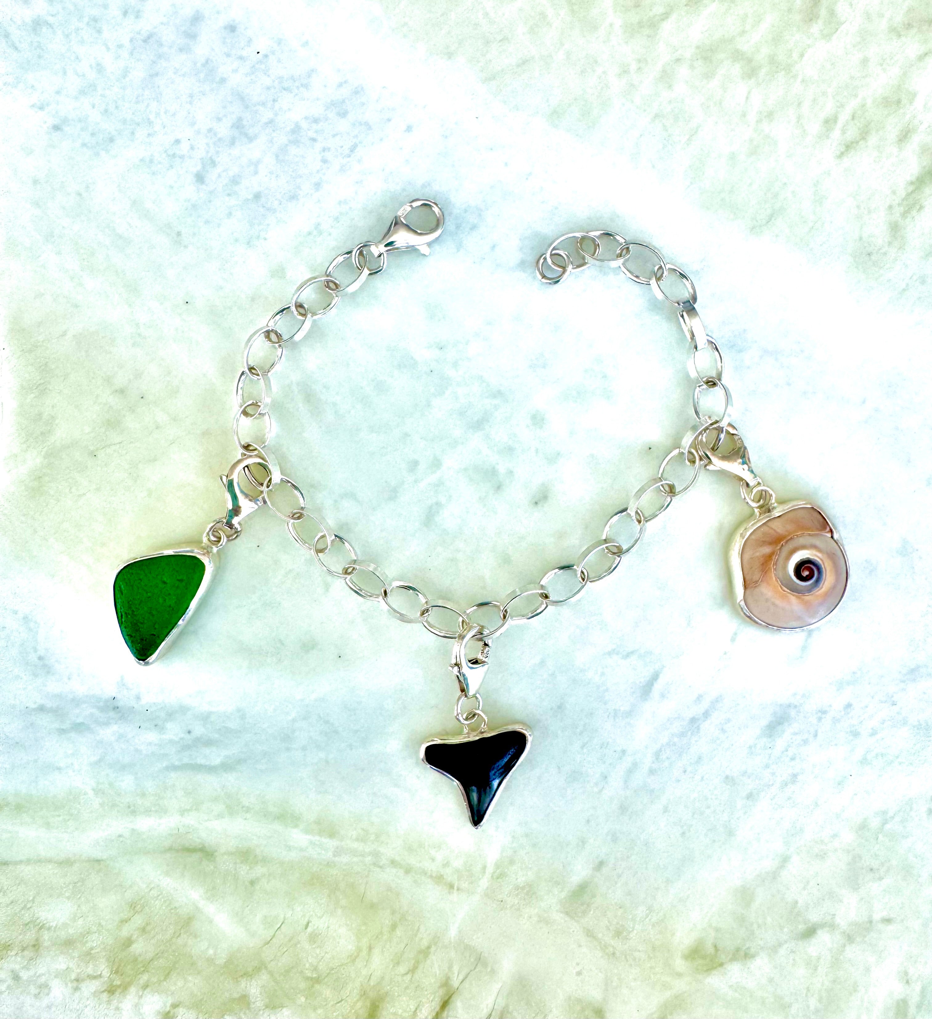 Sterling silver rolo link charm bracelet featuring green sea glass from Bonaire, shark eye shell, and fossilized shark tooth from Casey Key, Florida.