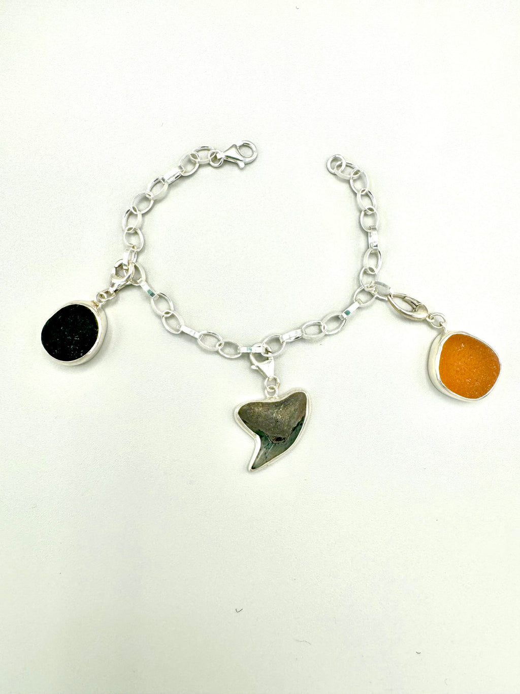 Historic charm bracelet featuring Sicilian red-glow black sea glass, fossilized shark tooth, and amber sea glass from England, set in sterling silver.