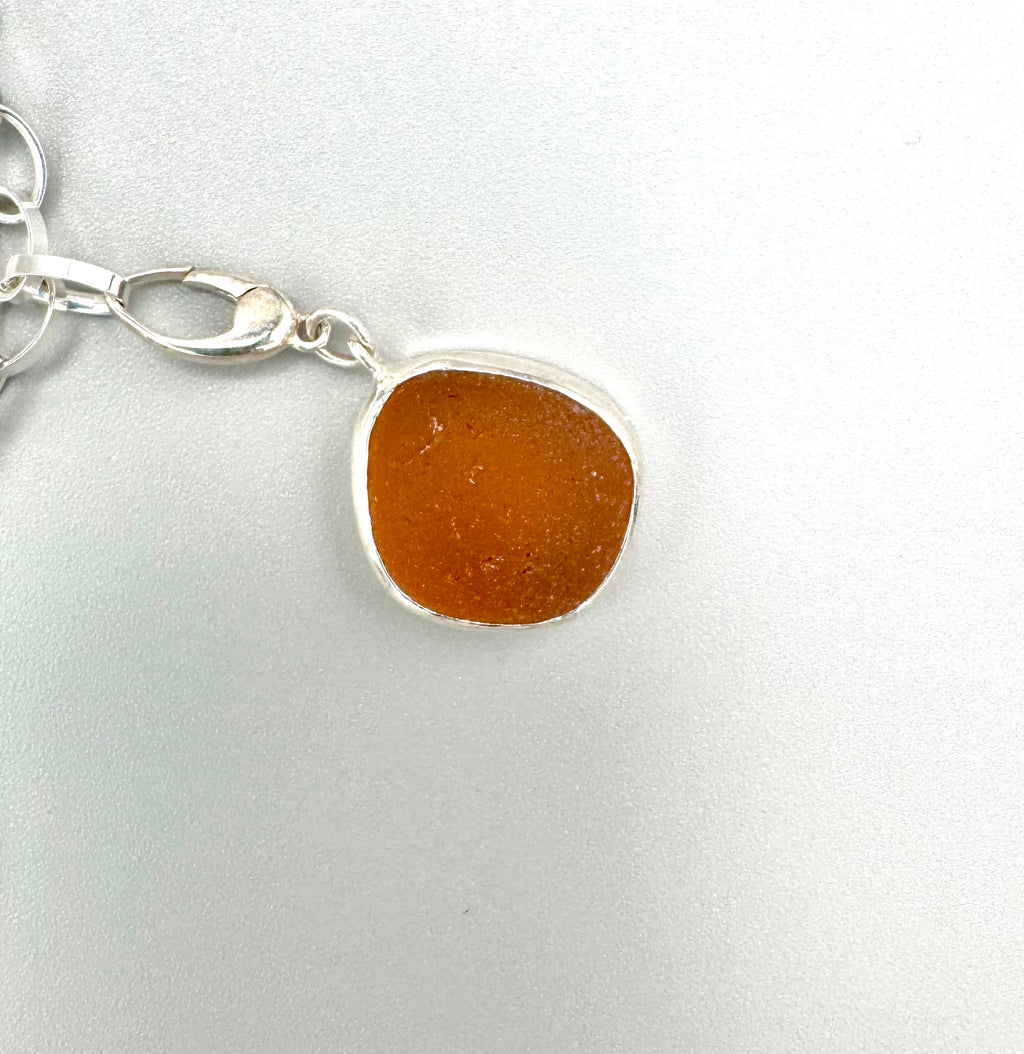 Historic charm bracelet featuring Sicilian red-glow black sea glass, fossilized shark tooth, and amber sea glass from England, set in sterling silver.