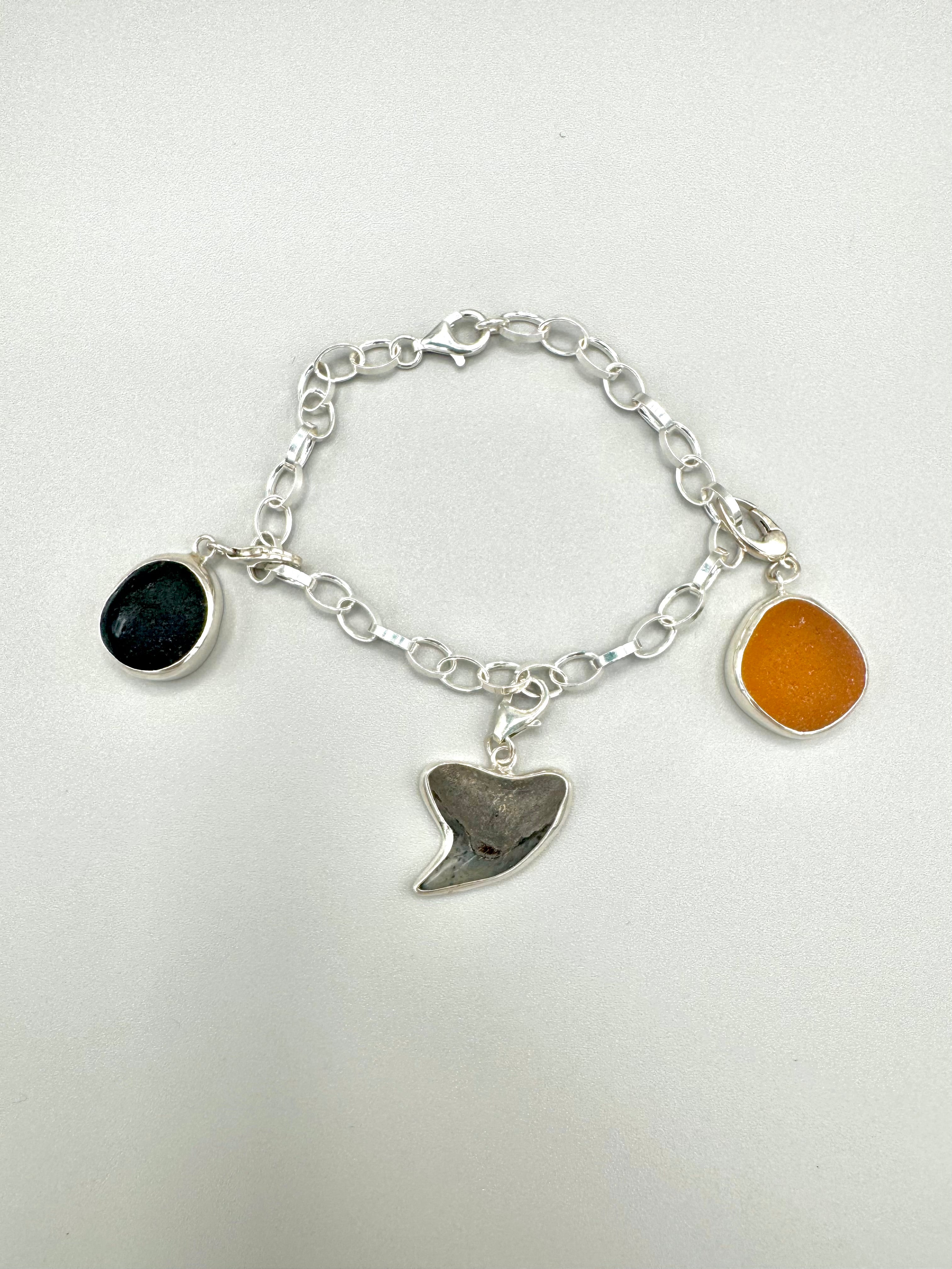 Historic charm bracelet featuring Sicilian red-glow black sea glass, fossilized shark tooth, and amber sea glass from England, set in sterling silver.