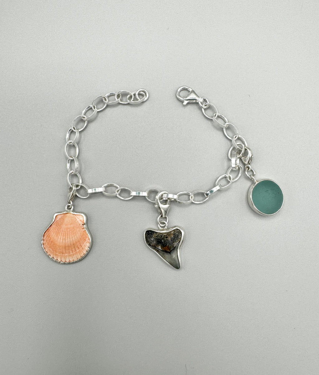 Sterling silver charm bracelet with pink scallop shell, fossilized shark tooth, and aquamarine sea glass from Japan — ocean-inspired handcrafted jewelry.