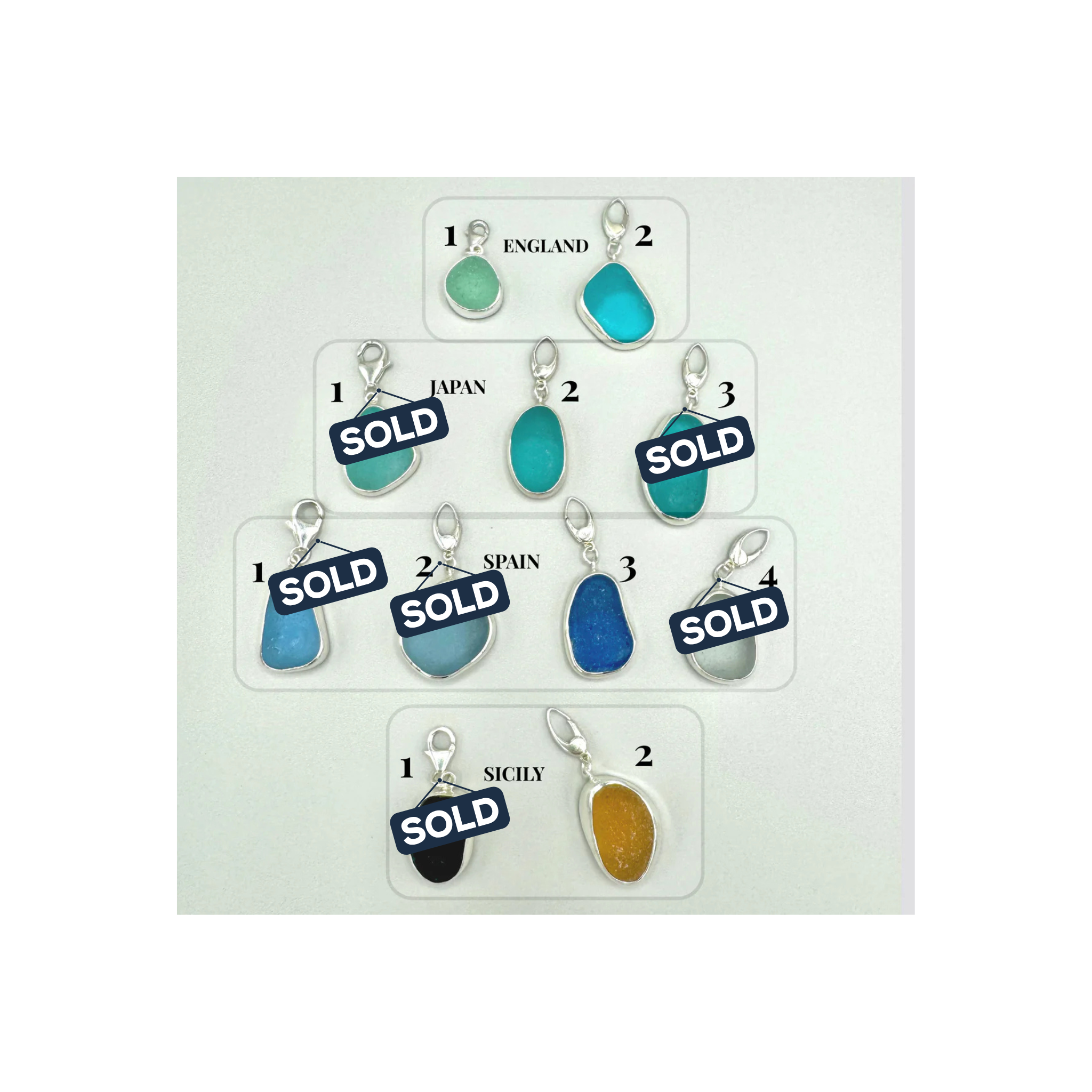 Collection of blue and green sea glass pendants with 'SOLD' labels on a white card.