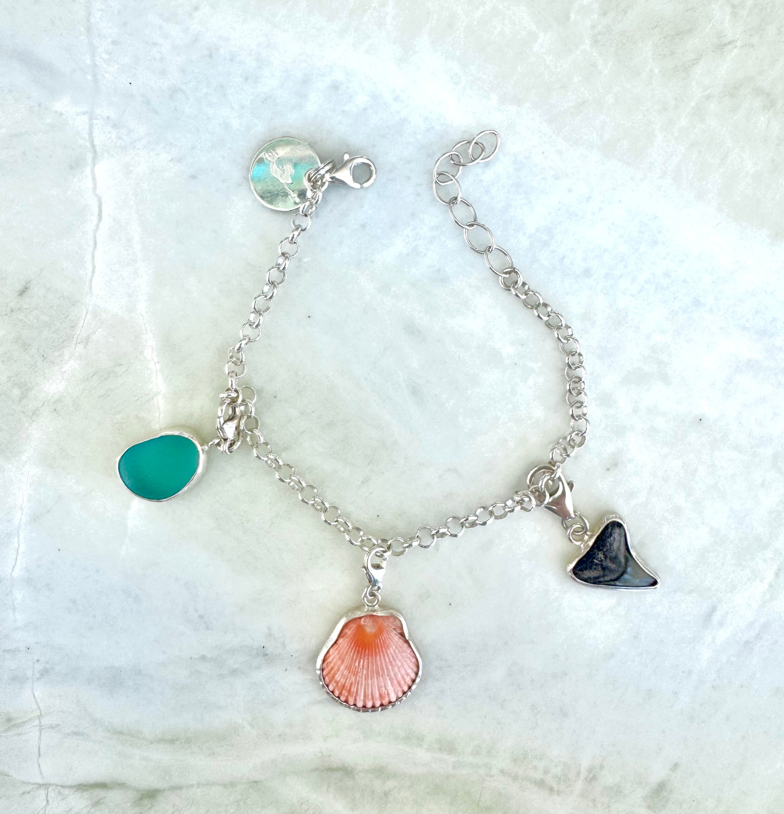 Sterling silver charm bracelet featuring aquamarine sea glass from Japan, pink scallop shell, and fossilized shark tooth from Casey Key, Florida.