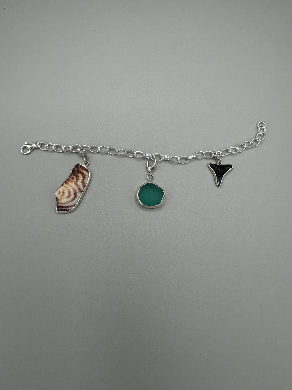 Sterling silver charm bracelet featuring seafoam green sea glass, fossilized shark tooth, and turkey wing shell.