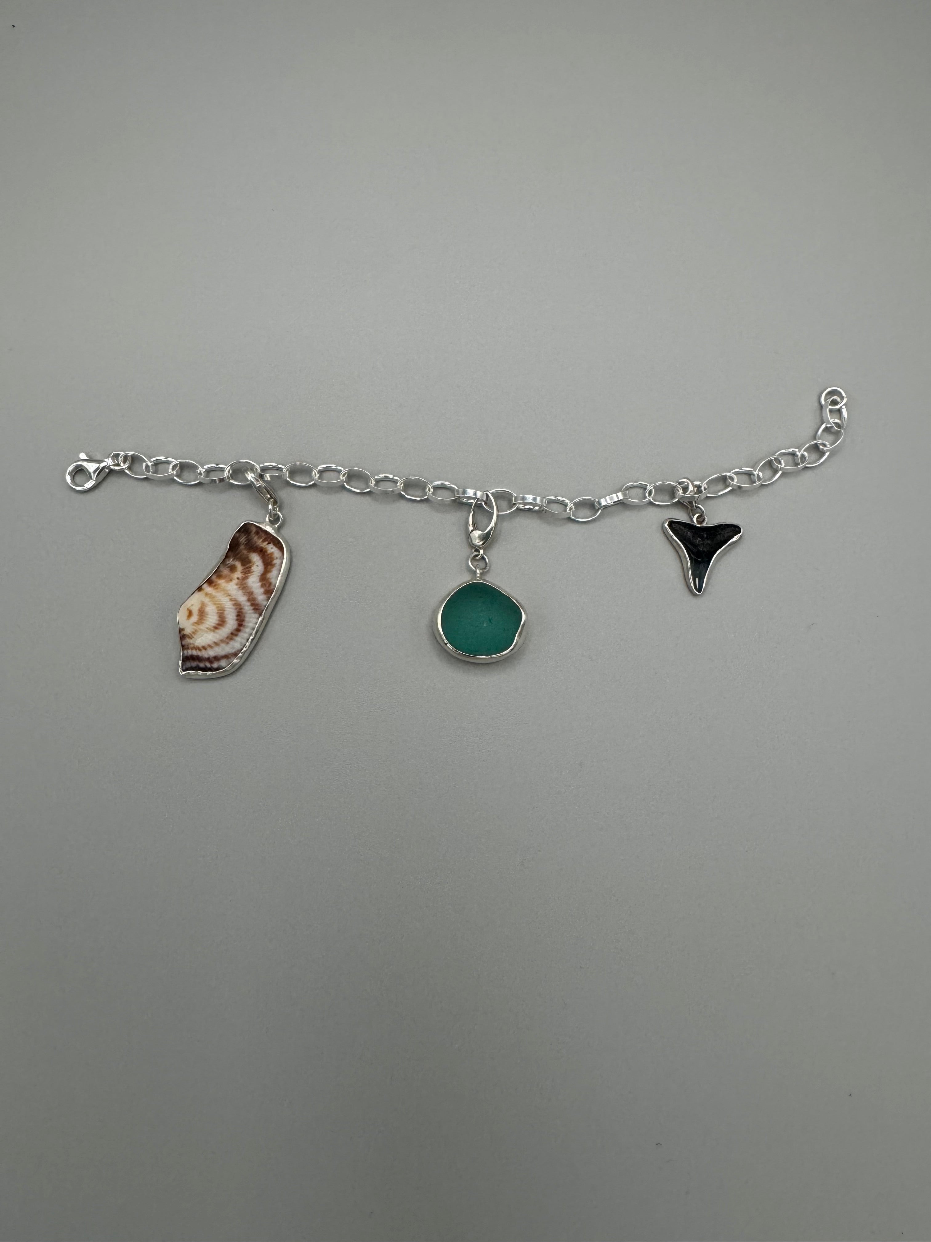 Sterling silver charm bracelet featuring seafoam green sea glass, fossilized shark tooth, and turkey wing shell.
