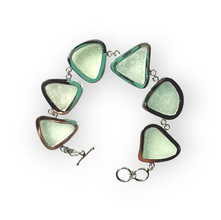 A handcrafted adjustable bracelet featuring six pieces of natural seafoam sea glass from the Adriatic Coast of Italy, bezel set in sterling silver with a toggle clasp, glowing softly under natural light.