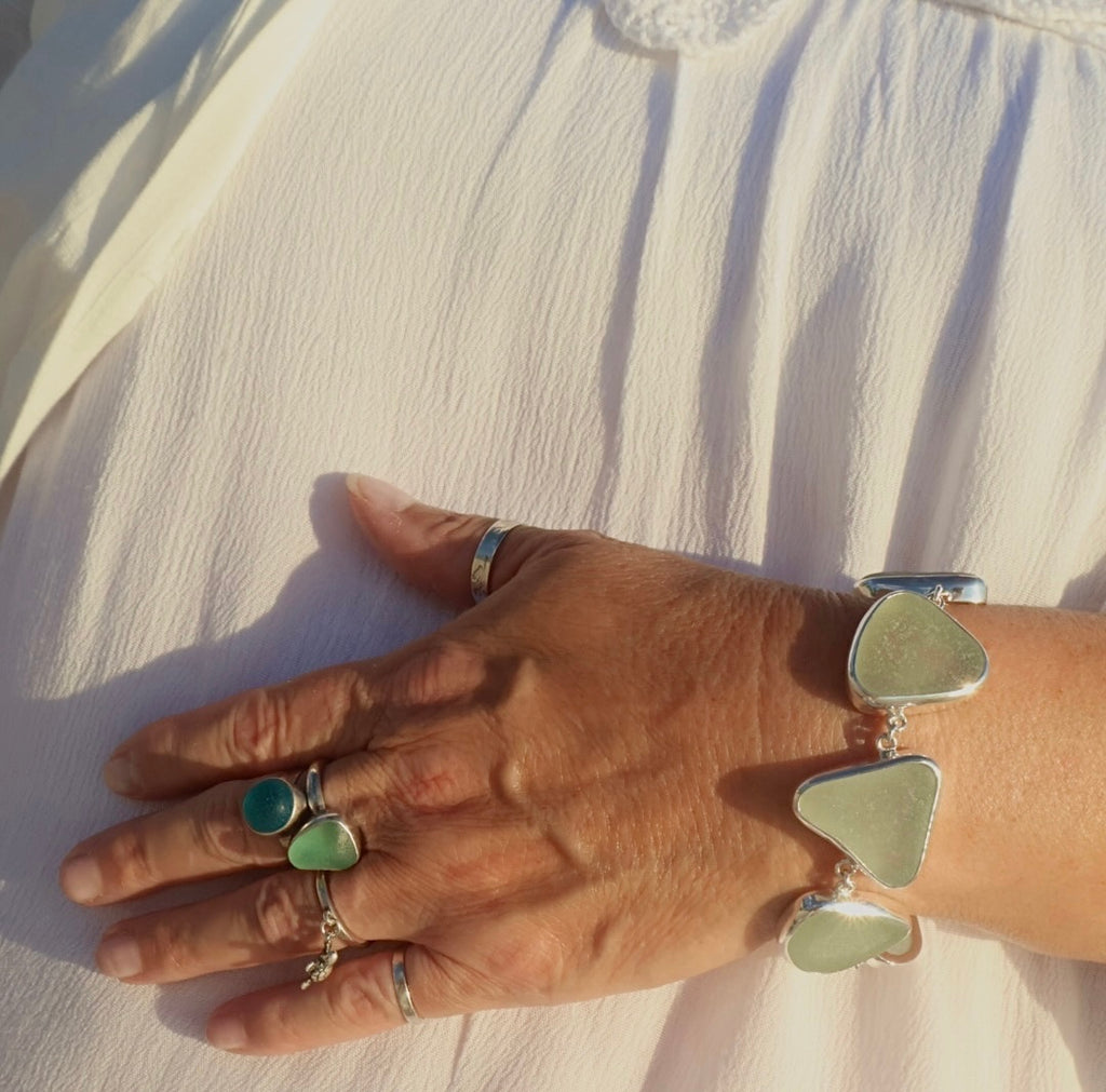 A handcrafted adjustable bracelet featuring six pieces of natural seafoam sea glass from the Adriatic Coast of Italy, bezel set in sterling silver with a toggle clasp, glowing softly under natural light.