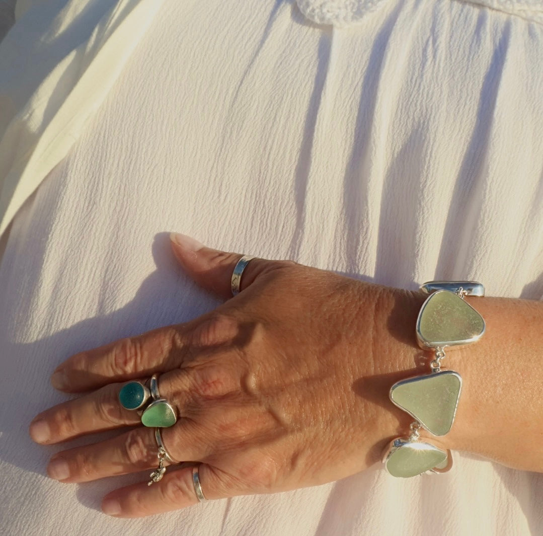 A handcrafted adjustable bracelet featuring six pieces of natural seafoam sea glass from the Adriatic Coast of Italy, bezel set in sterling silver with a toggle clasp, glowing softly under natural light.
