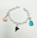 Sterling silver charm bracelet featuring a shark eye shell, fossilized shark tooth, and turquoise Mediterranean sea glass — handcrafted ocean-inspired jewelry.”