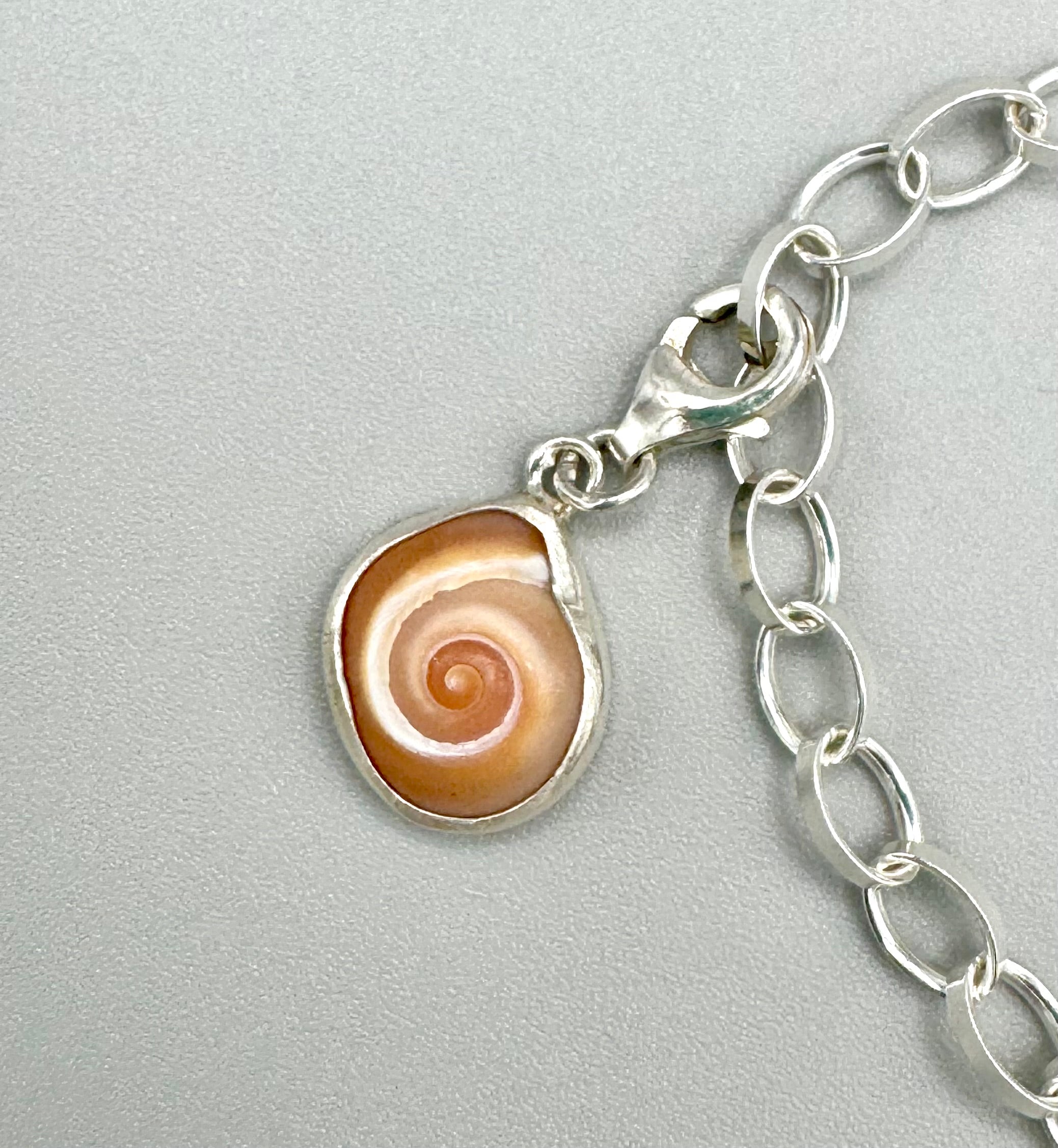 Sterling silver charm bracelet featuring a shark eye shell, fossilized shark tooth, and turquoise Mediterranean sea glass — handcrafted ocean-inspired jewelry.”