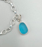 Sterling silver charm bracelet featuring a shark eye shell, fossilized shark tooth, and turquoise Mediterranean sea glass — handcrafted ocean-inspired jewelry.